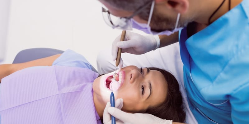 Dentist examining a female patient with tools describes dental emergency.