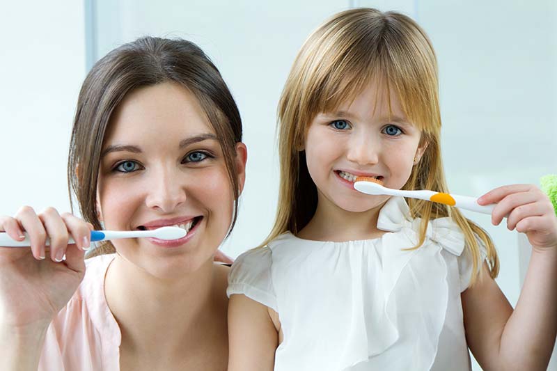 A smiling mother and daughter brushing their teeth together importance for good dental health.