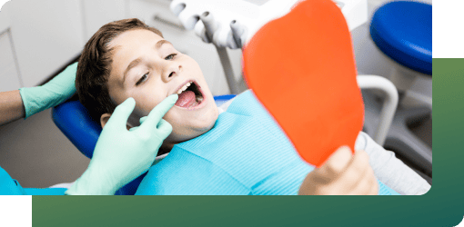 A dentist examining a boy’s teeth in a dental chair with a mirror, conducting a final pediatric orthodontics assessment for lasting results.