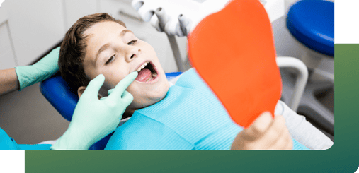 A dentist examining a boy’s teeth in a dental chair with a mirror, conducting a final pediatric orthodontics assessment for lasting results.