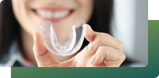 A woman holds a clear mouthguard, showcasing general dental services for bruxism protection and sports safety.
