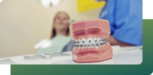 A dental model with braces on a table, with a dentist and patient in the background, discussing dental braces adjustments for optimal alignment.