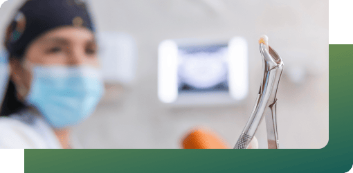 Dental professional in a mask and cap holding a tool with extracted wisdom teeth after removal.