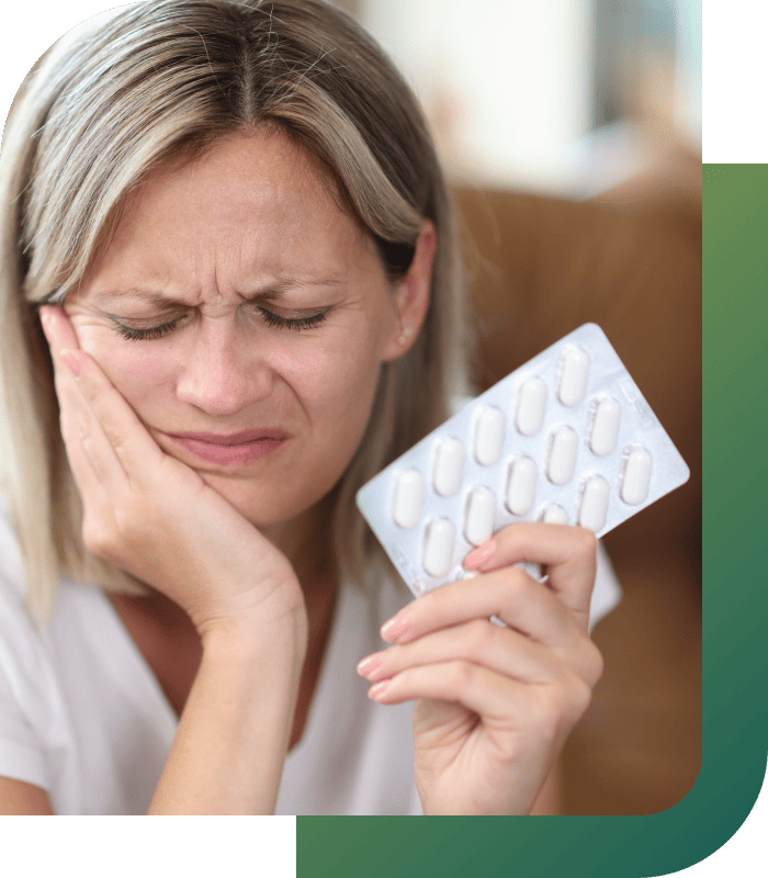 A woman holding pills in one hand while expressing discomfort from tooth pain.