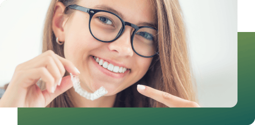 A smiling woman with glasses pointing to her clear aligner, preparing to wear retainers to maintain long-term results.