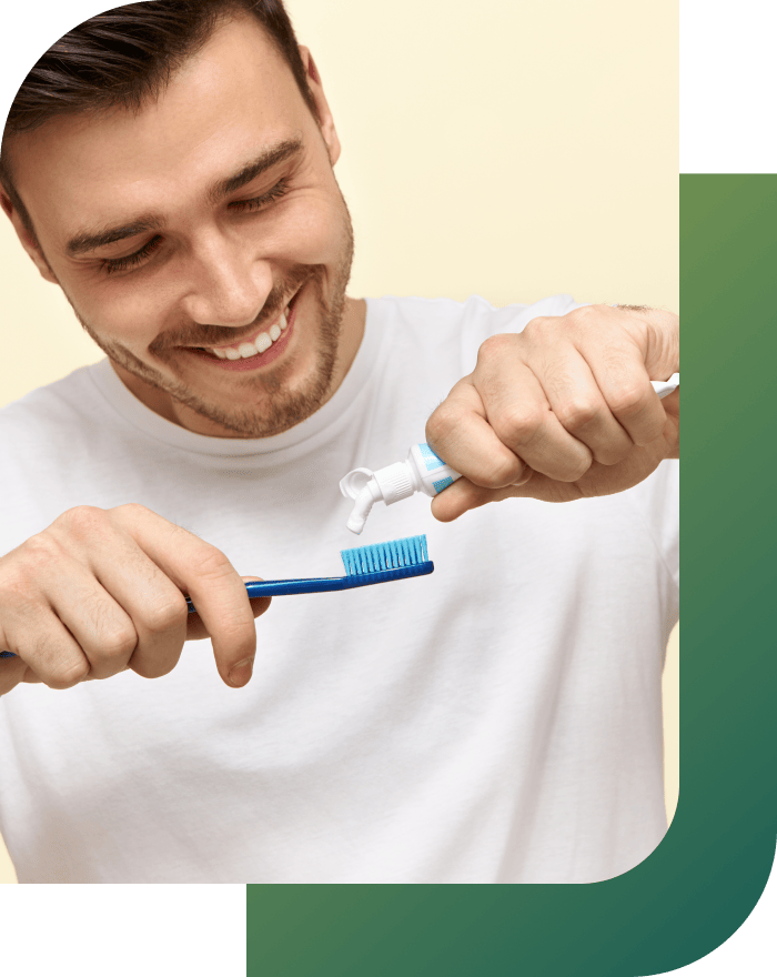 A happy person applying toothpaste to a toothbrush in the correct way.