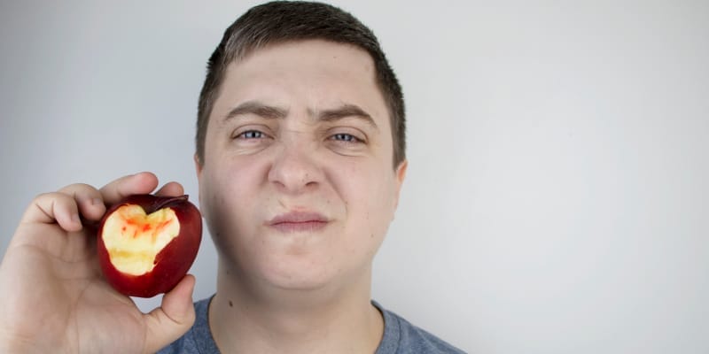 A man in pain and a blood-stained bitten apple symbolize the signs of gum disease.