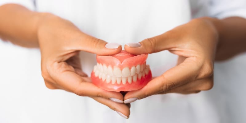 Removable denture held by gloved hands during a dental hygiene procedure